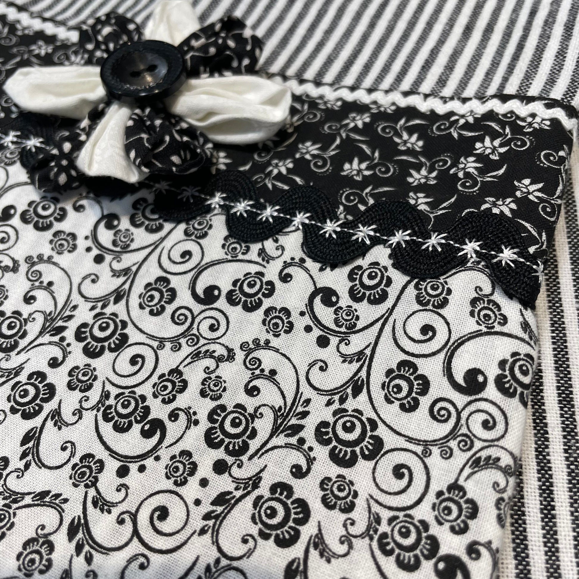 Black and white retro farmhouse tea towel. Featuring black and white striped toweling. Black and white floral quilting cotton accents with white and black ric rac, a handcrafted flower with button center and embroidery stitching. Part of a coordinating collection of farmhouse decor. Browse the entire collection. Then head over to the Home Stitchery Decor YouTube Channel for more Farmhouse DIY Decor Fun. See you there!