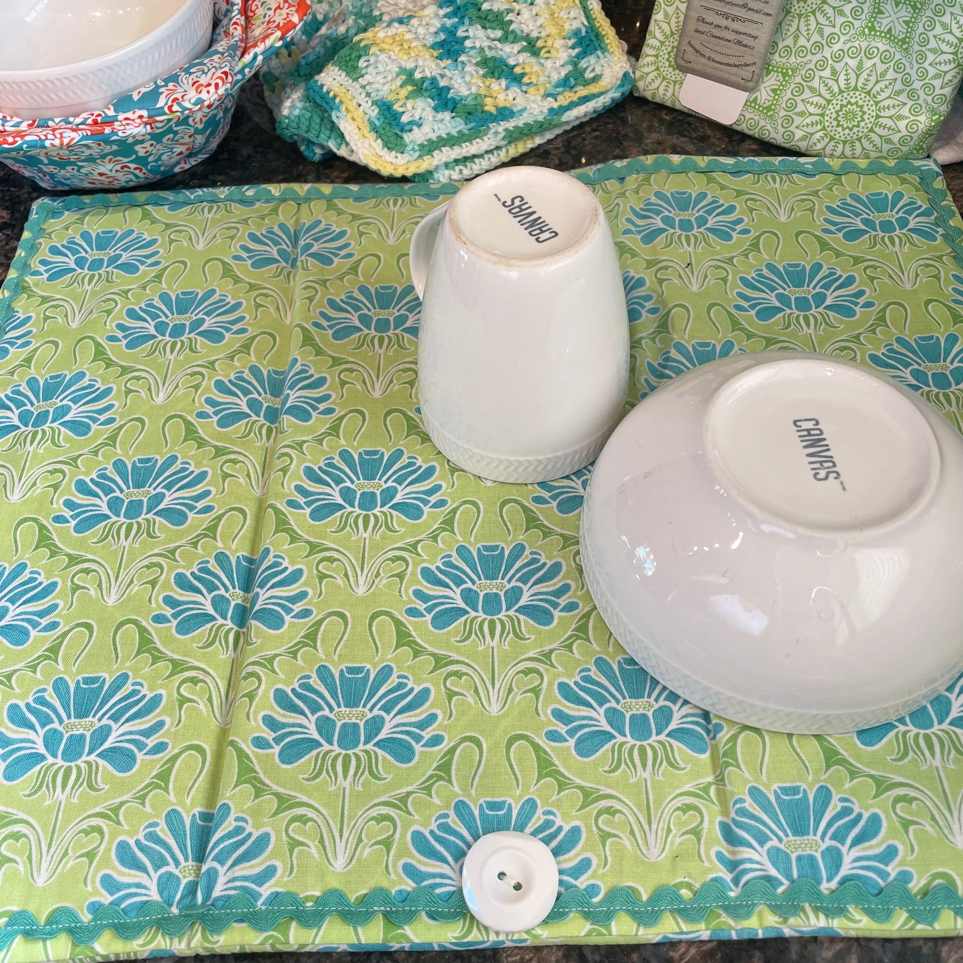 Teal and Green handcrafted dish drying mat. Featuring teal flowers, ric rac and a white button. Part of a coordinated collection of kitchen linens. Shop the collection, or follow along on with sewing and 3d Layered Mandala tutorials on the Home Stitchery Decor YouTube Channel